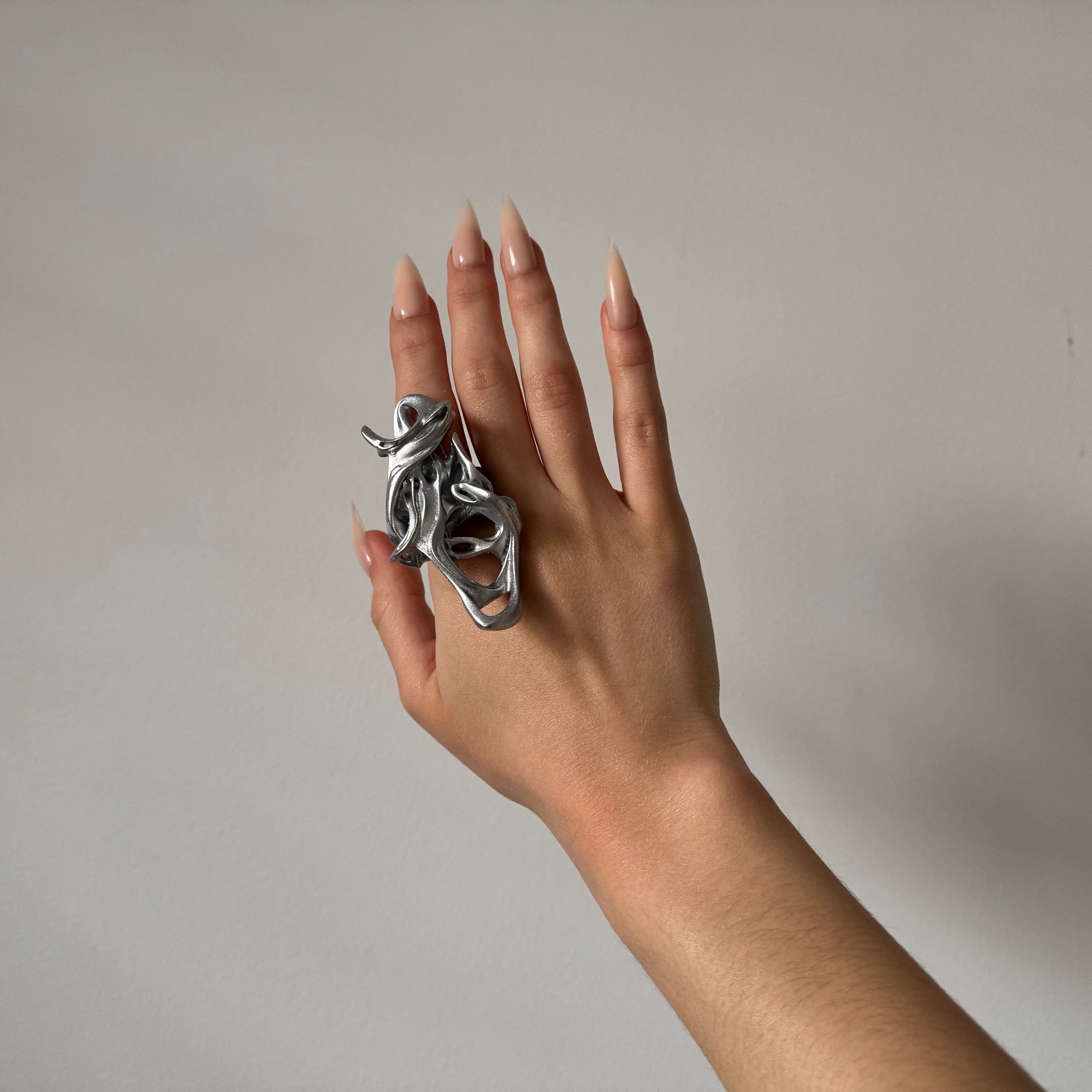 Hand wearing a unique silver ring on a plain background
