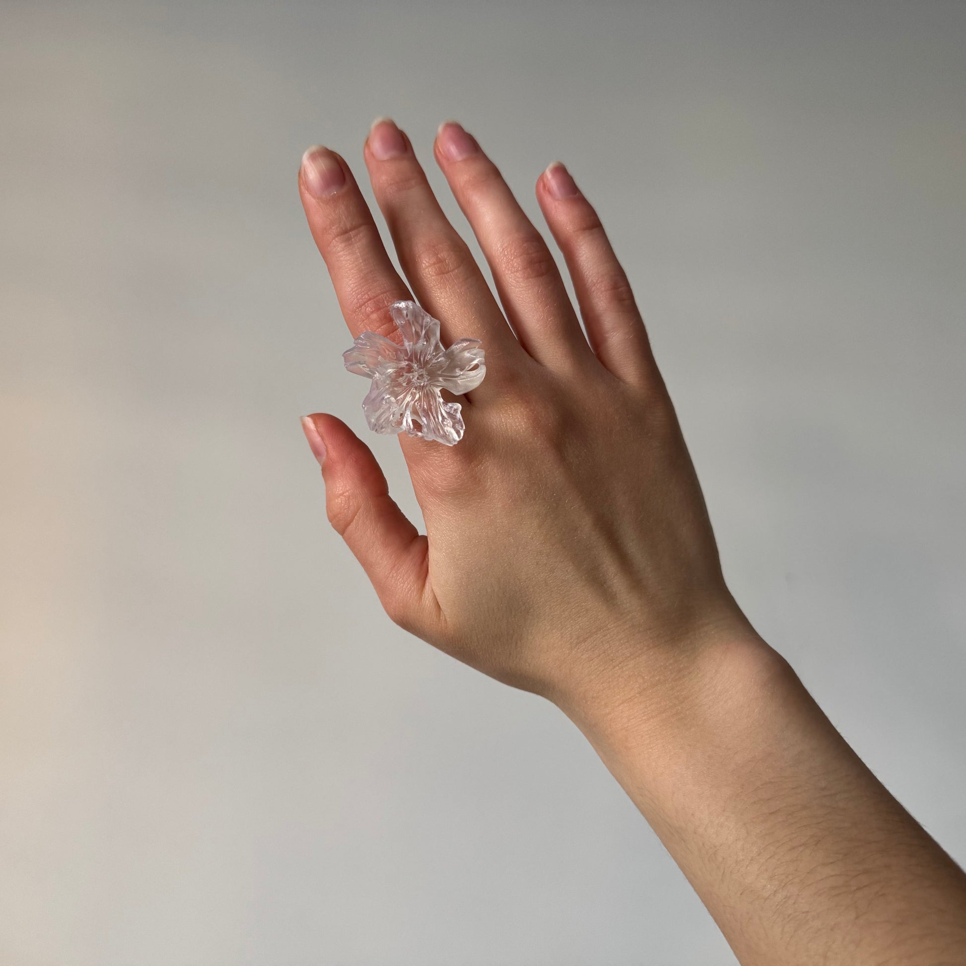 Hand wearing a clear floral ring on a plain background