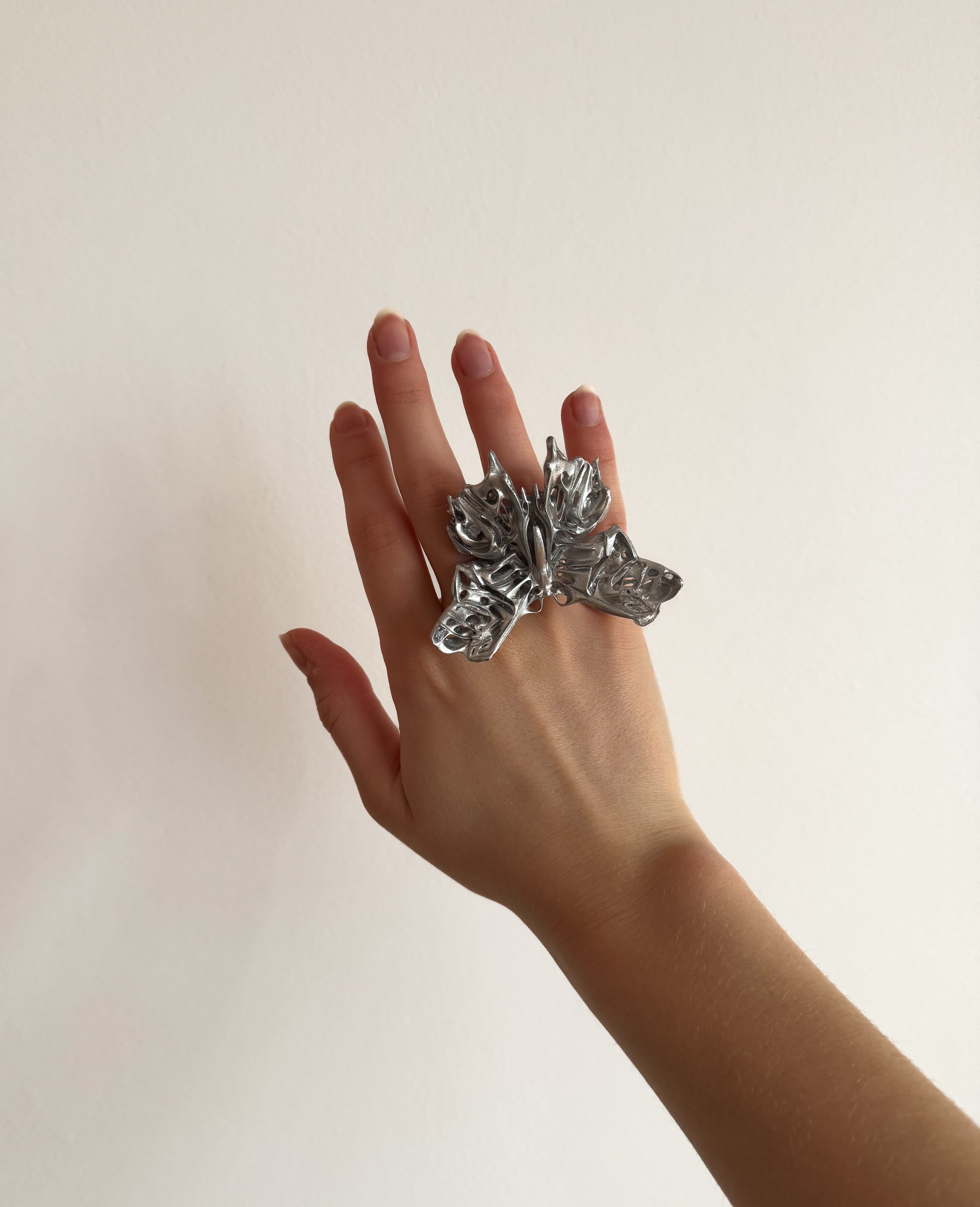 Hand wearing a statement 3D printed butterfly ring on a plain background