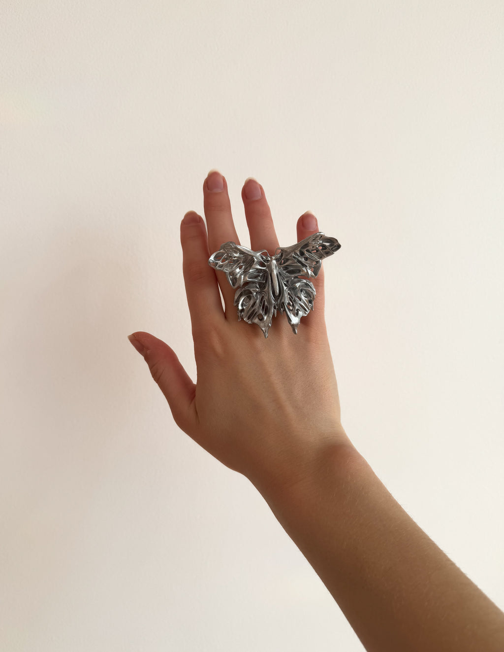 Hand wearing a statement 3D printed butterfly ring on a plain background