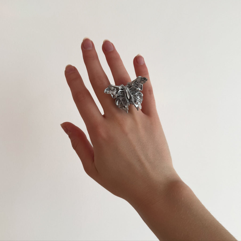 Hand wearing a silver statement butterfly-shaped ring on a plain background