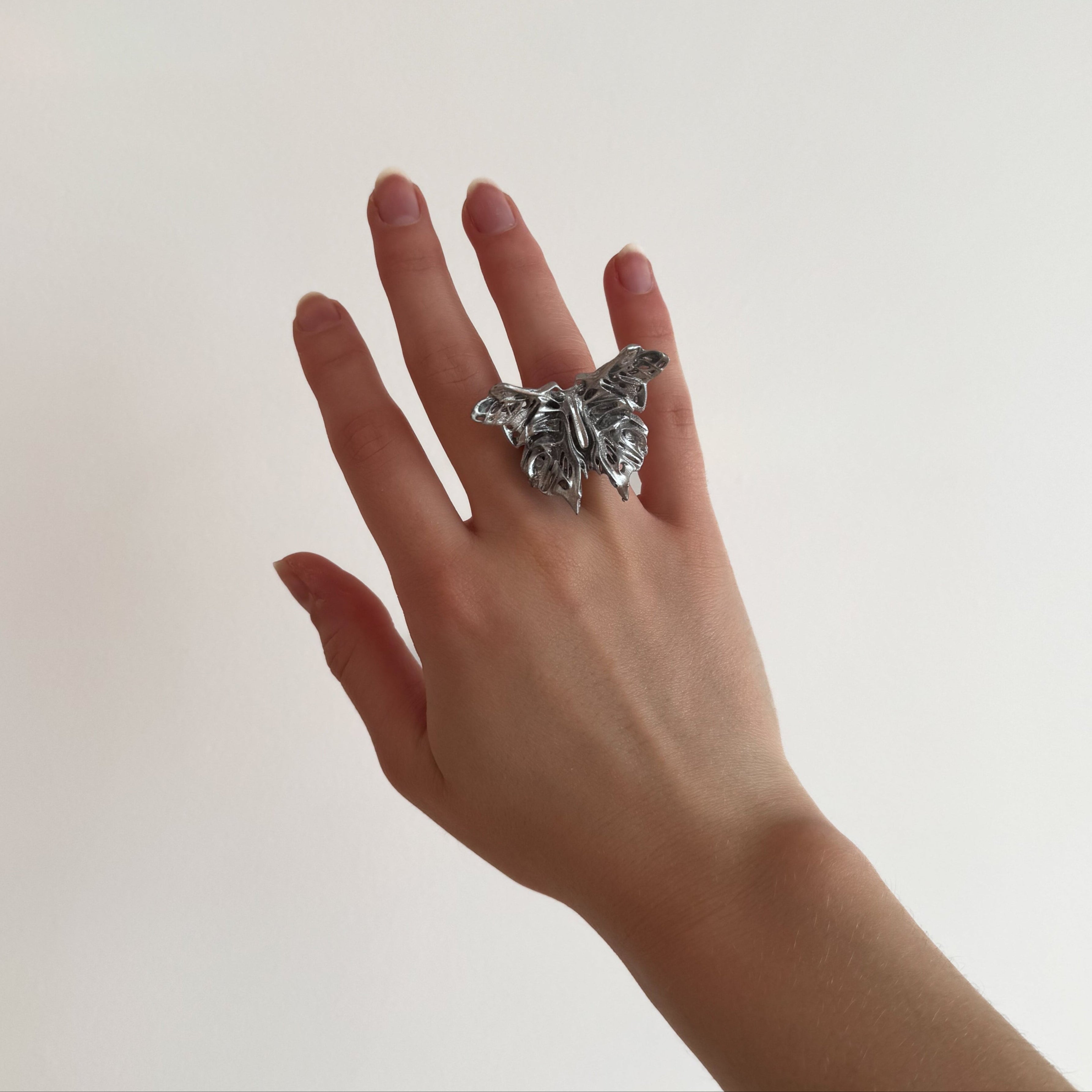 Hand wearing a silver statement butterfly-shaped ring on a plain background