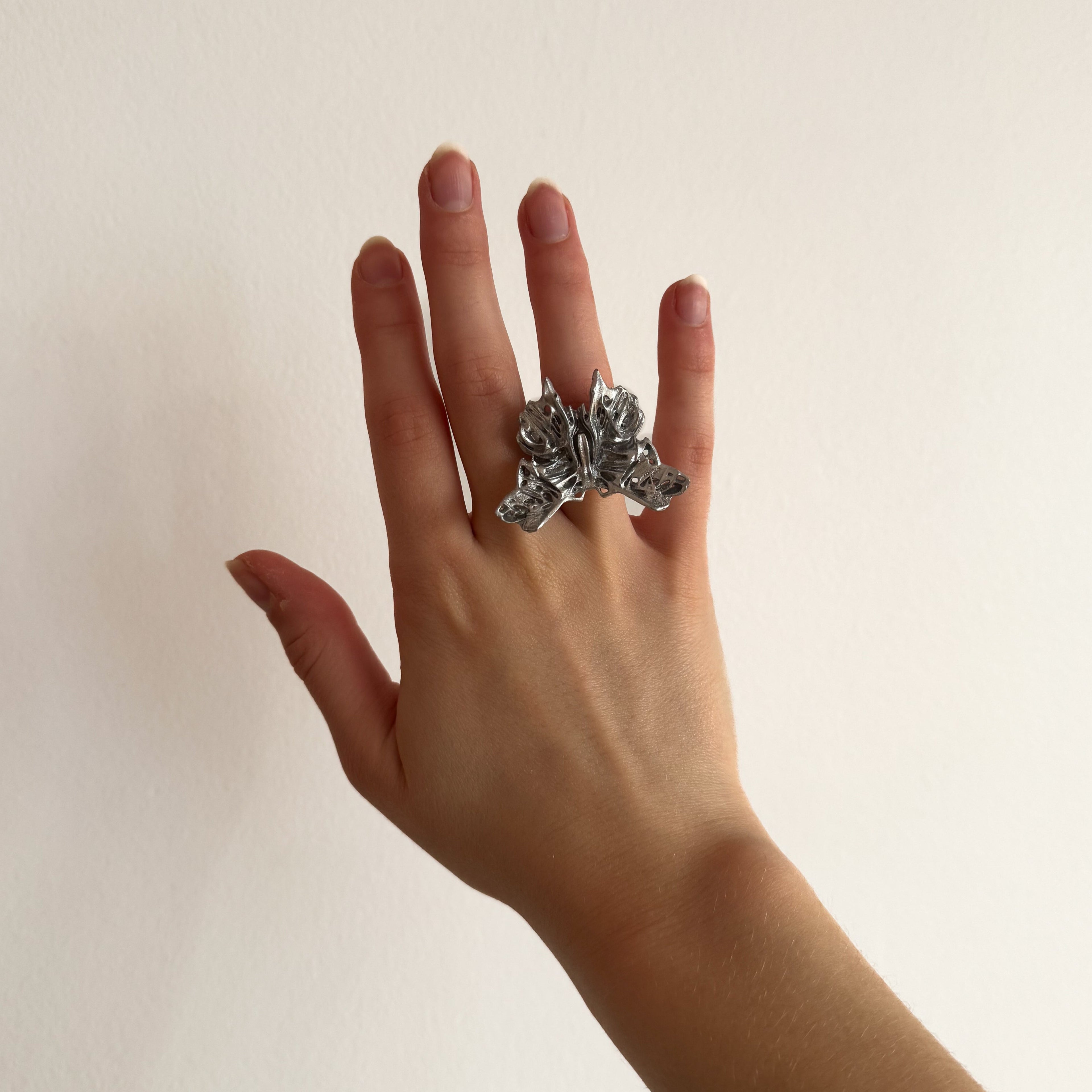 Hand wearing a silver statement butterfly-shaped ring on a plain background