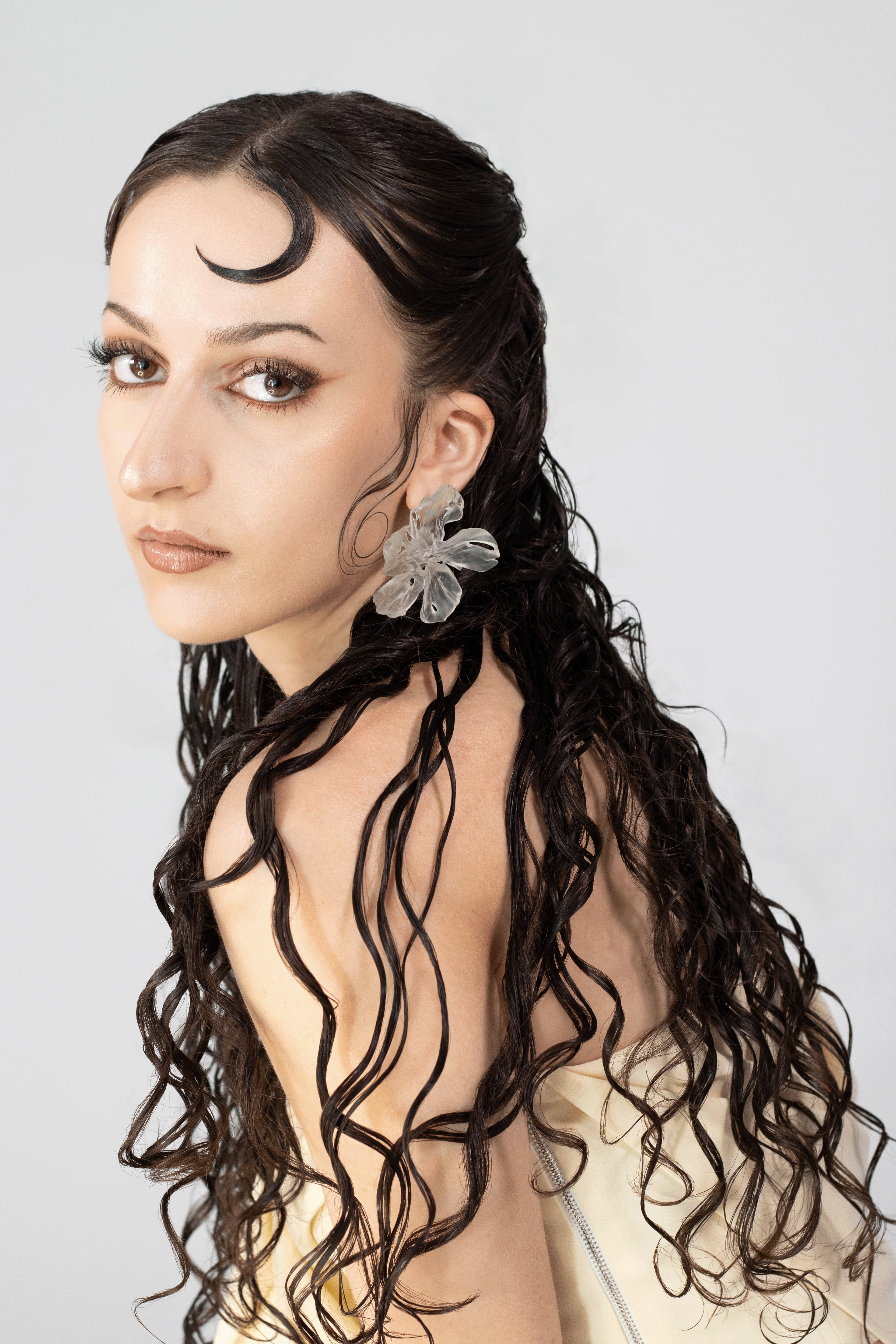Woman with long, wavy hair wearing a floral statement 3D printed clear earring