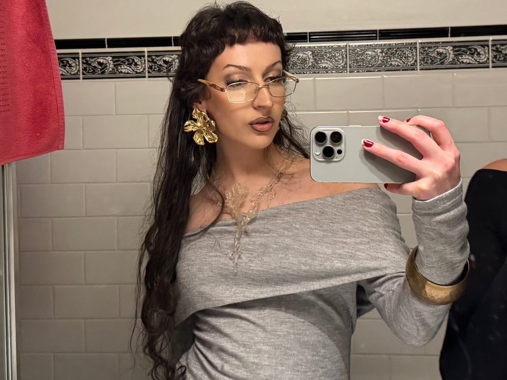 Woman taking a mirror selfie in a bathroom wearing large gold abstract flower earrings
