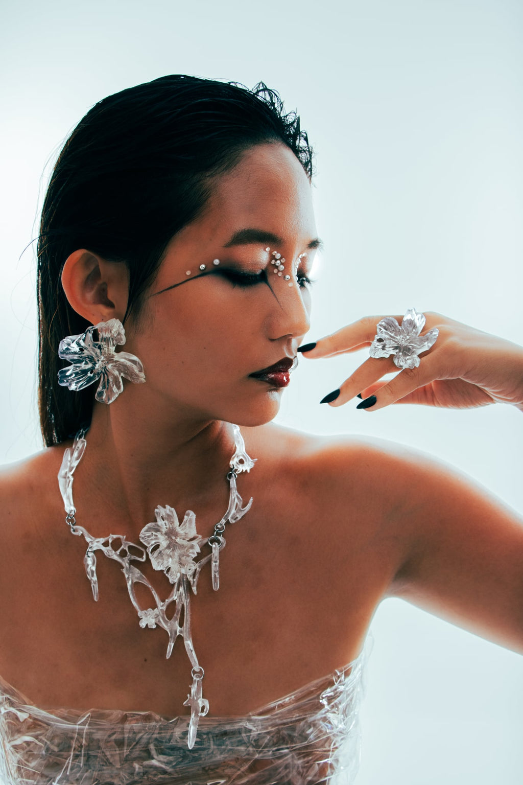 Woman wearing large, ornate statement clear gloss translucent 3d printed earrings, necklace, and ring.