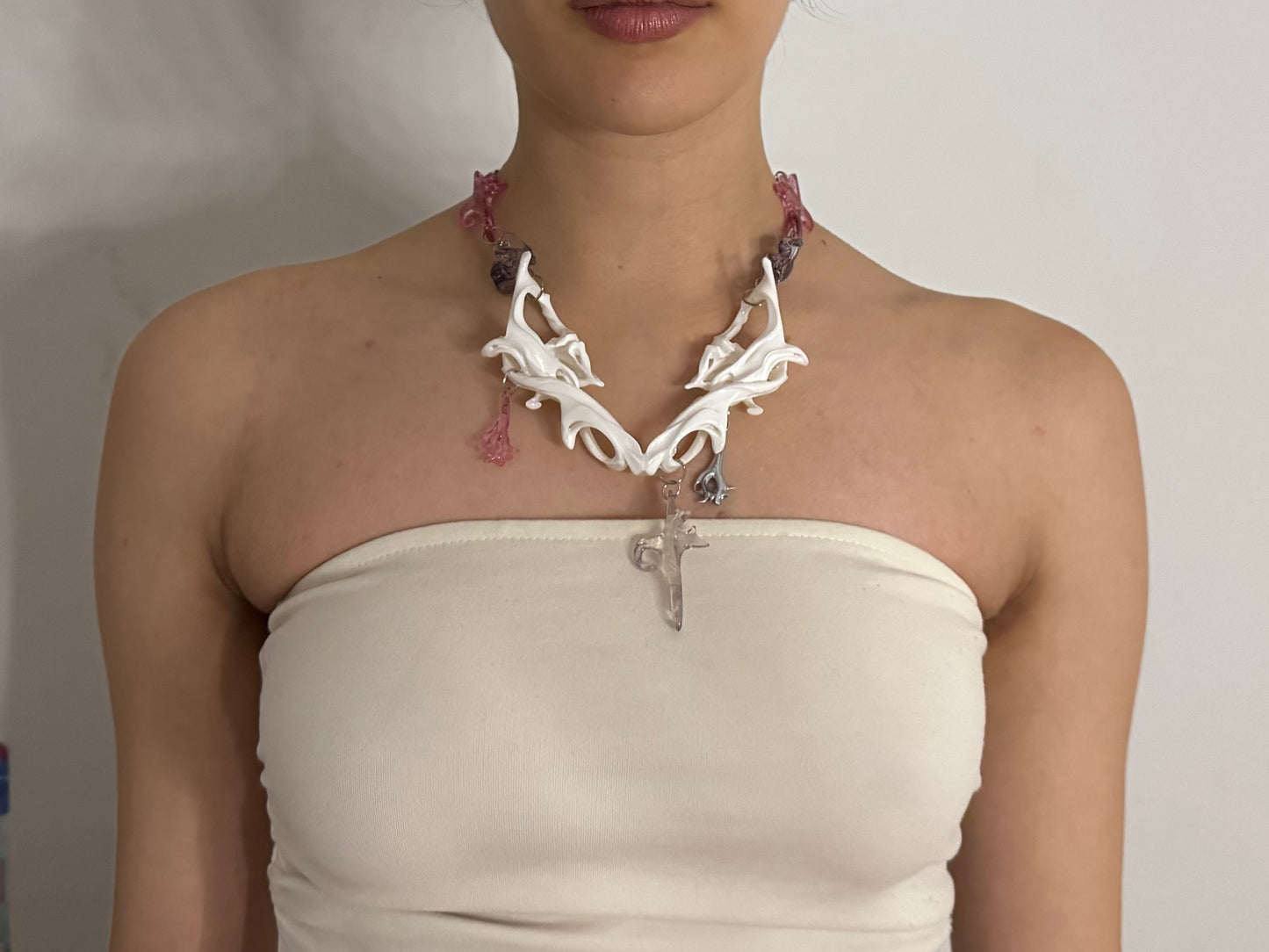 Person wearing a white necklace with pink and purple accents on a plain background