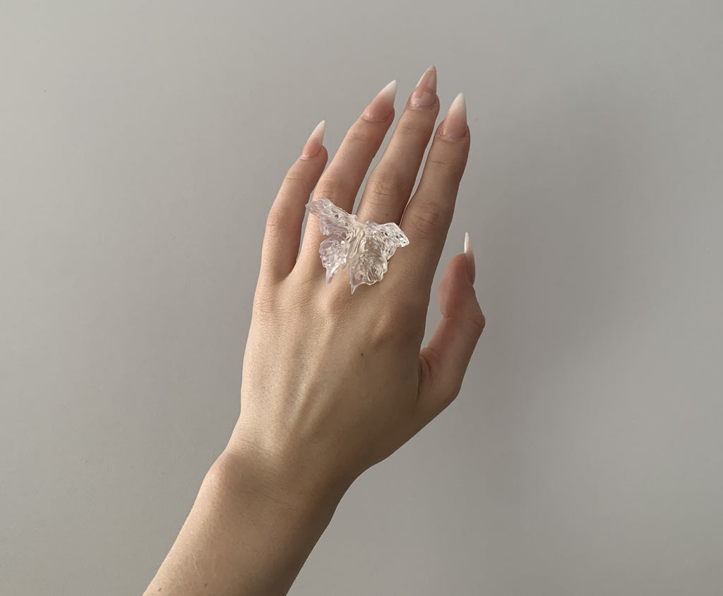 Hand wearing a large, unique butterfly 3D printed ring against a neutral background